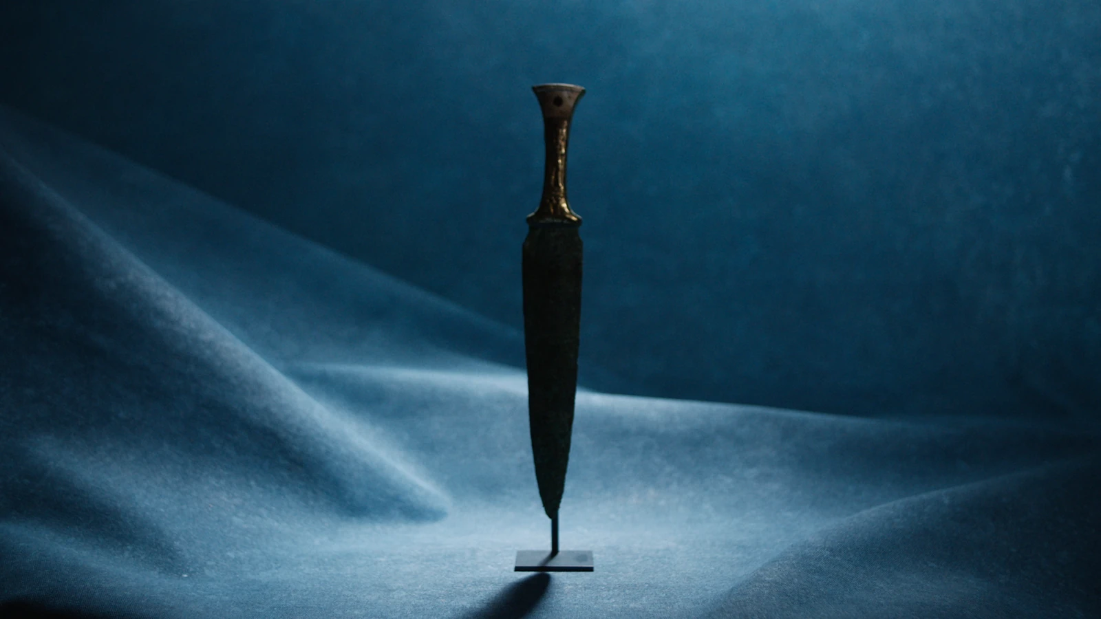 An ancient dagger displayed against blue fabric.