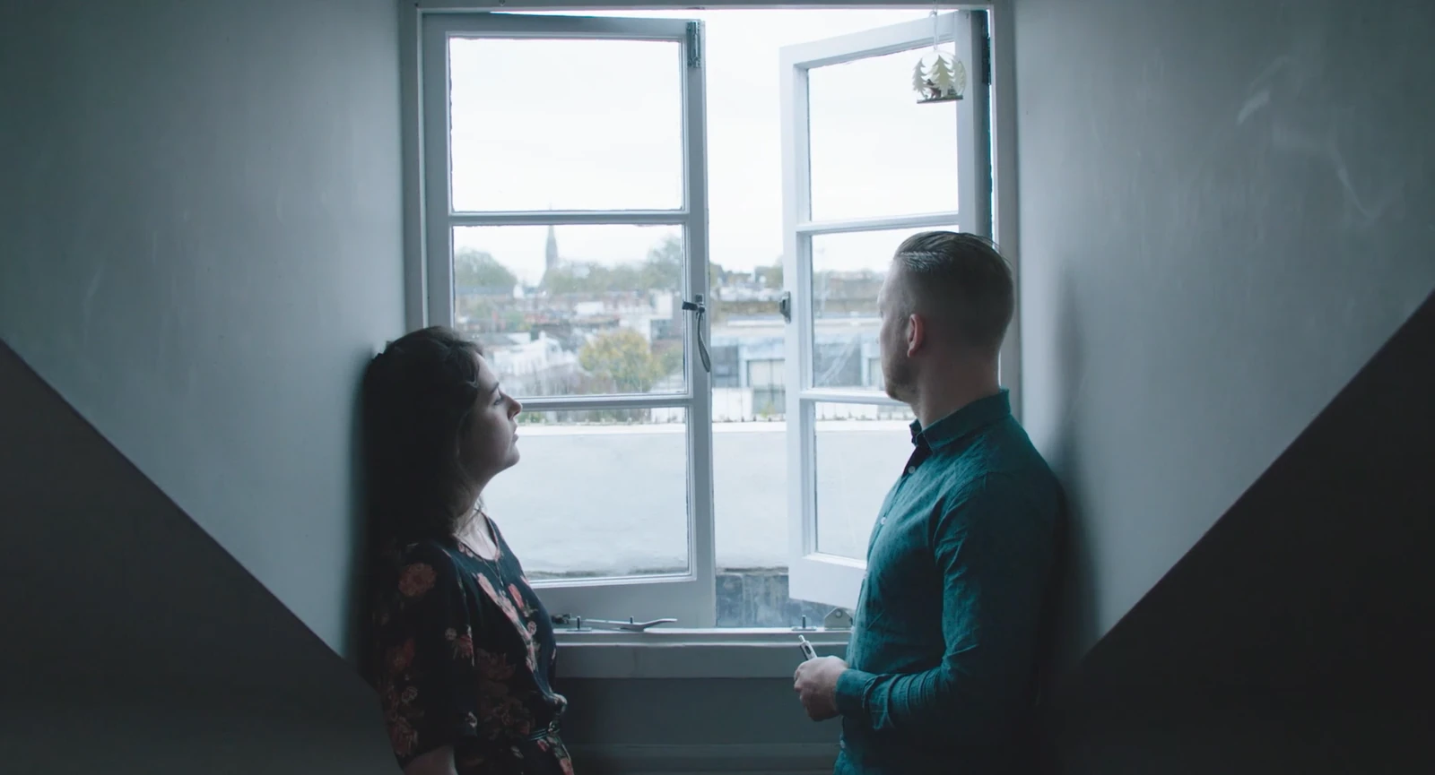 Two people facing one another beside an open window.
